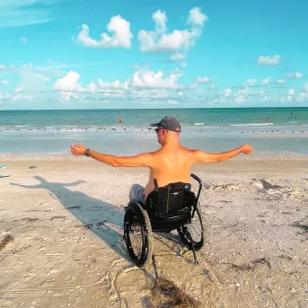 Typ, der im Rollstuhl am Strand sitzt