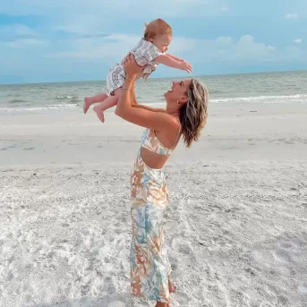mom lifting young kid above her head on the beach smiling