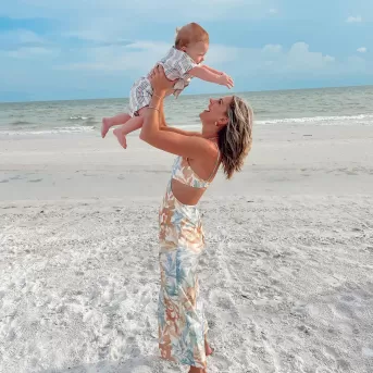 Mutter hebt lächelnd ihr kleines Kind über ihren Kopf am Strand