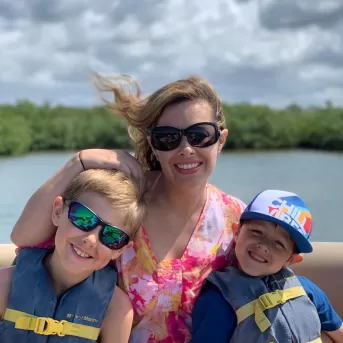 Mamá con dos hijos en un barco con chalecos salvavidas puestos.