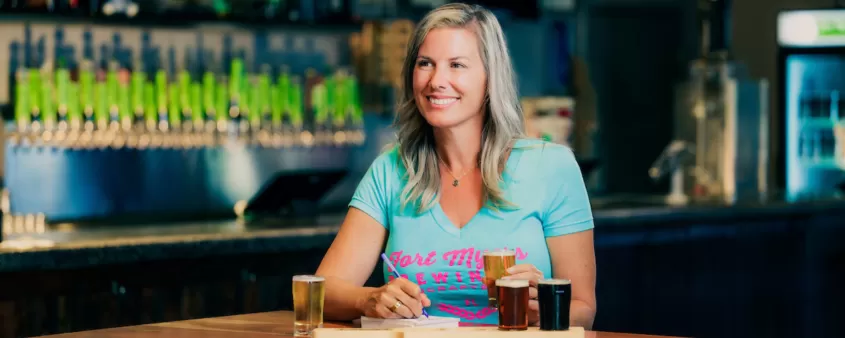 A woman sits at a high top table at Fort Myers Brewing Co with a flight of beer