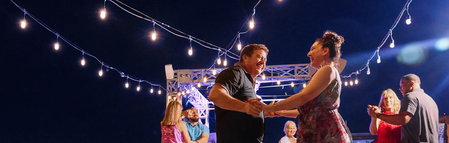 Couple dances salsa beneath string lights.