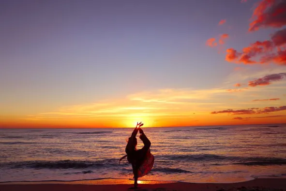 A woman does yoga on the beach at sunset
